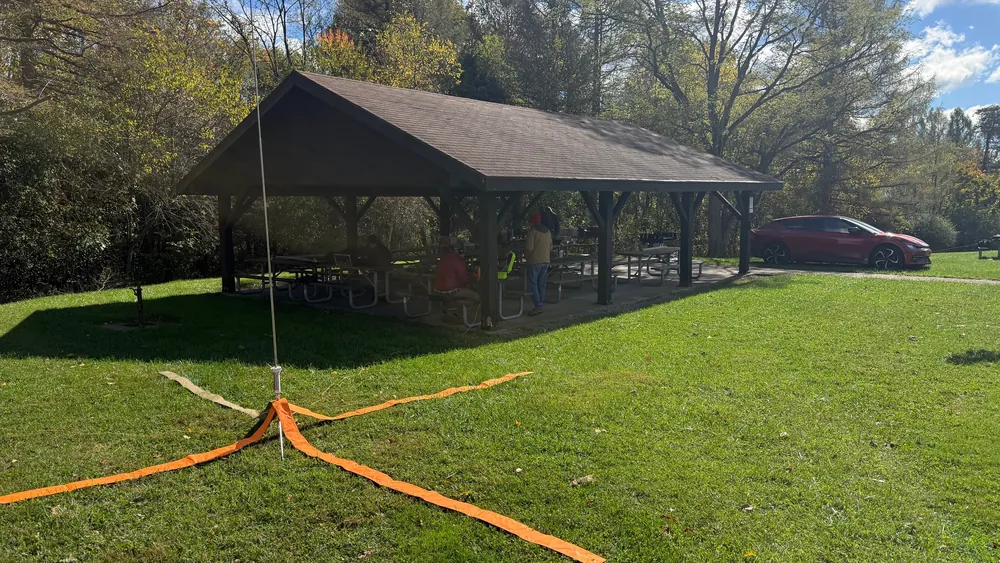 A portable vertical antenna with orange radials beside a park pavilion